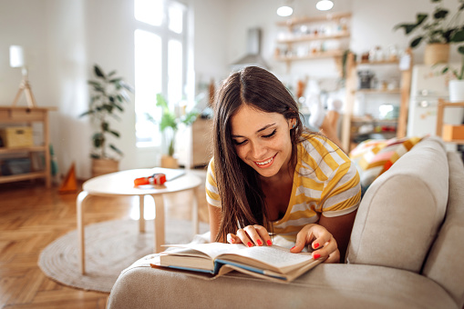 Shot of a young woman reading a book while relaxing at home