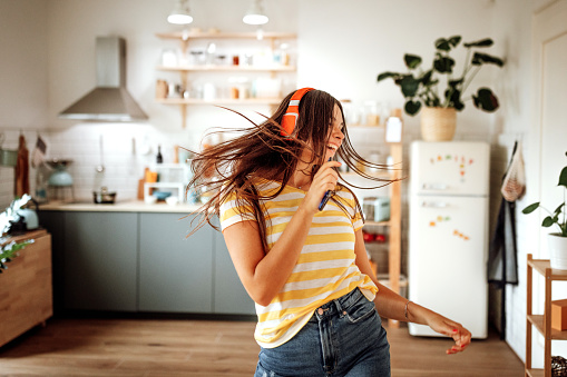 Beautiful young woman listening to music on headphones at her cozy apartment