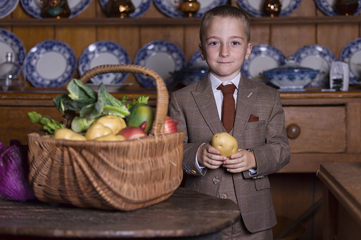 Smartly dressed boy examining a basket of vegetables for quality.
