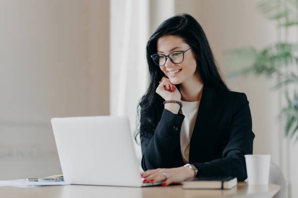 istock Cheerful female employee types on laptop computer, works remotely, concentrated with smile at device screen, writes email letter, works in office drinks coffee uses new application. Technology concept 1409461331