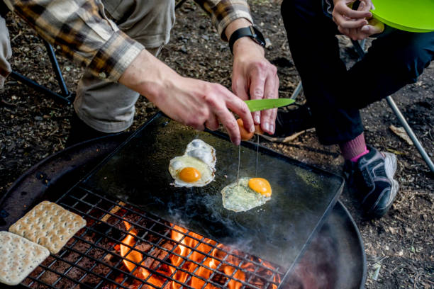 istock Breakfast camp cooking. Man cooking grilling eggs and warming bread on a cast iron plate over the camp fire. Camping lifestyle 1409462561