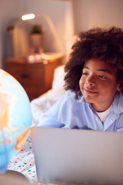 istock Boy In Bedroom At Night Lying On Bed Using With Laptop With Illuminated Globe 1409462943