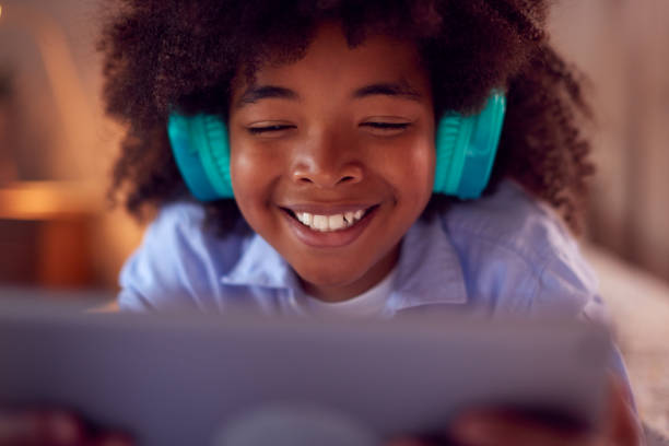 istock Boy In Bedroom Lying On Bed Wearing Headphones Using Digital Tablet 1409462948