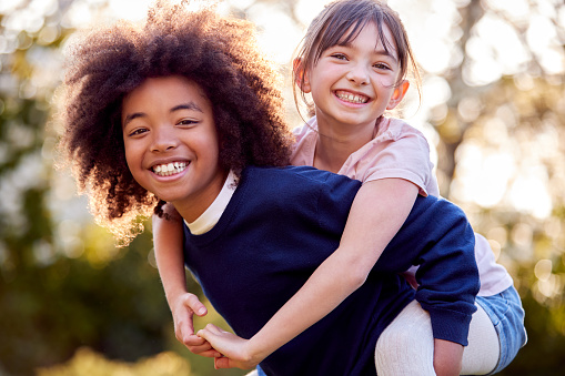 Portrait Of Smiling Boy Giving Girl Piggyback Outdoors In Garden