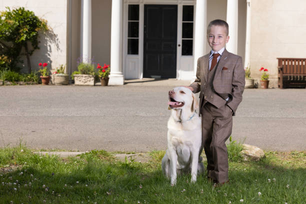Well dressed, upper class boy posing outside the manor house with his pet dog.