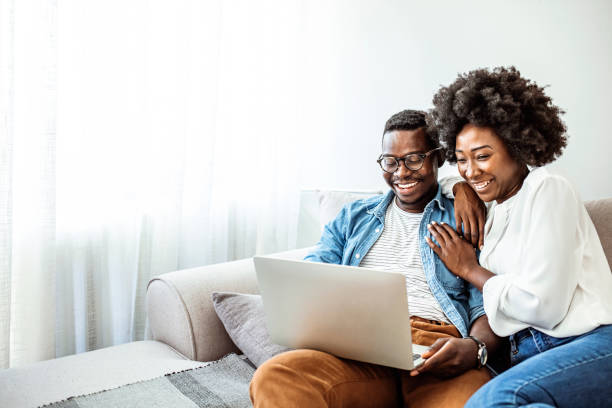 Attractive couple using laptop together on sofa to shop online at home stock photo