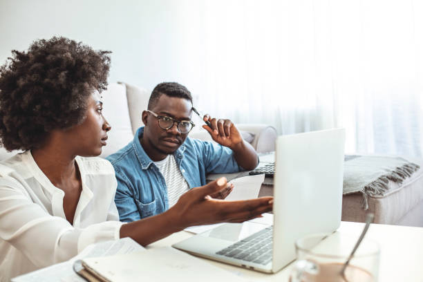 una pareja joven calculando sus facturas domésticas en casa. - home finances couple computer african ethnicity fotografías e imágenes de stock
