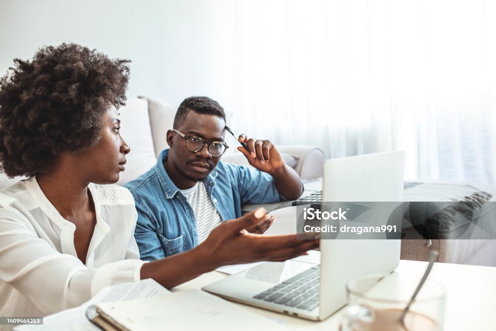 Young couple calculating their domestic bills at home. Young couple calculating their domestic bills at home. Young family discussing family finances. Serious worried african american couple reading documents consider mortgage loan insurance contract terms African-American Ethnicity Stock Photo