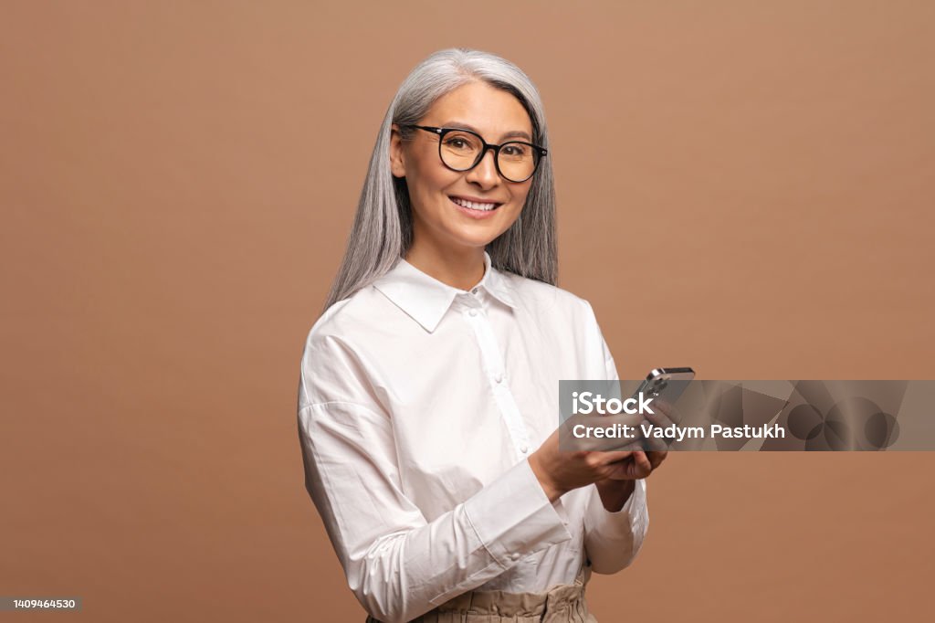 Happy business woman in formal shirt touching to the smartphone screen while feeling great with new phone features. Indoor studio shot isolated on beige Happy business woman in formal shirt touching to the smartphone screen while feeling great with new phone features. Indoor studio shot isolated on beige background One Woman Only Stock Photo