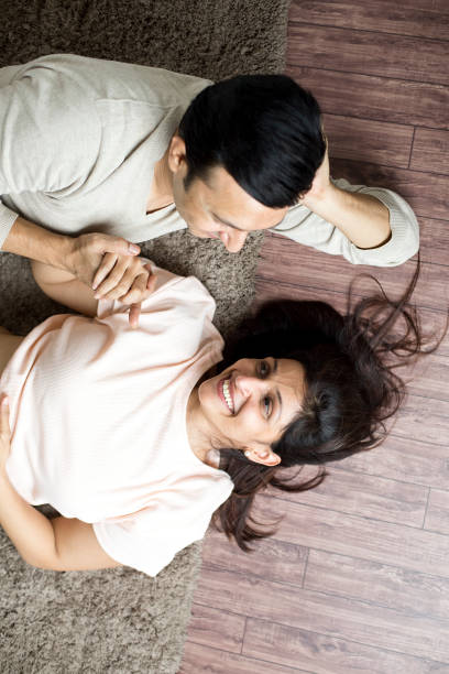 couple holding hands while lying down at home - couple loving lying on back carpet imagens e fotografias de stock