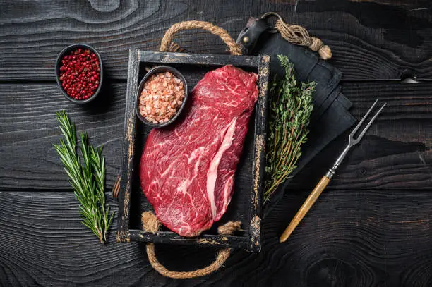 Unccoked rump steak or raw top sirloin beef meat steak. Black wooden background. Top view.