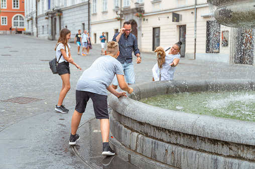 Family with two young children and a puppy having fun by the water fountain in the city.