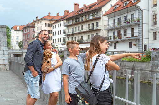 Cheerful family standing by the iron fence by the river in the city Ljubljana and enjoying the view.