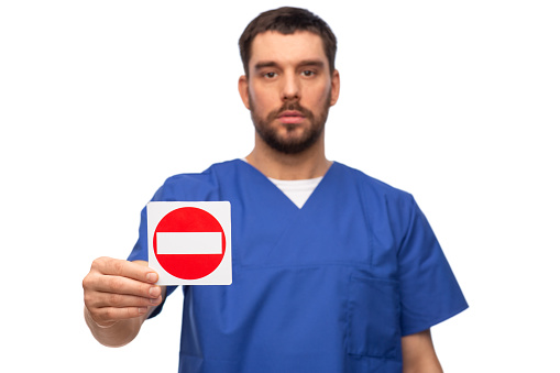 healthcare, profession and medicine concept - male doctor in blue uniform showing stop sign over white background