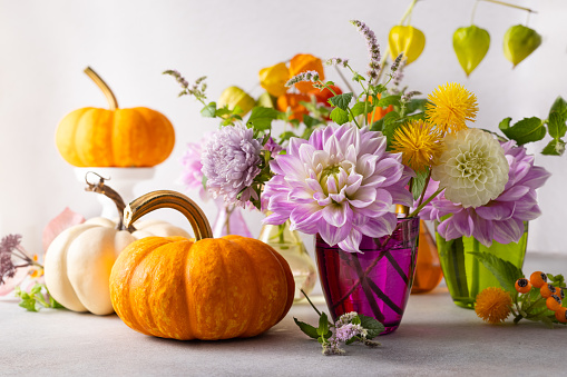 Autumn still life with bouquet of flowers and white and orange pumpkins on table. Autumn decoration for home.