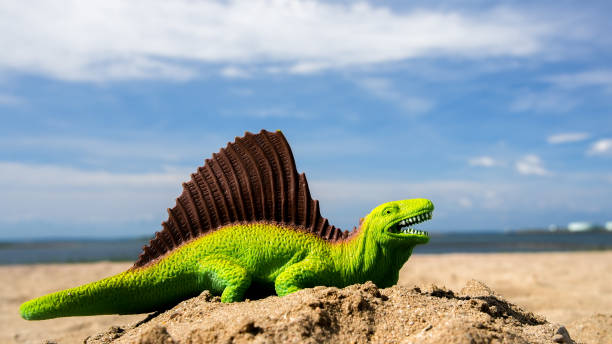 istock Green colored plastic dinosaur on beach with blue sky 1409471596