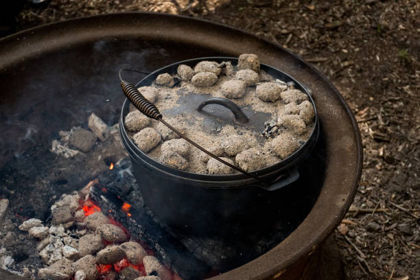 istock cast iron Dutch oven camp cooking with coal briquettes beads on top. Campfire in a firepit. Camping cooking 1409472211