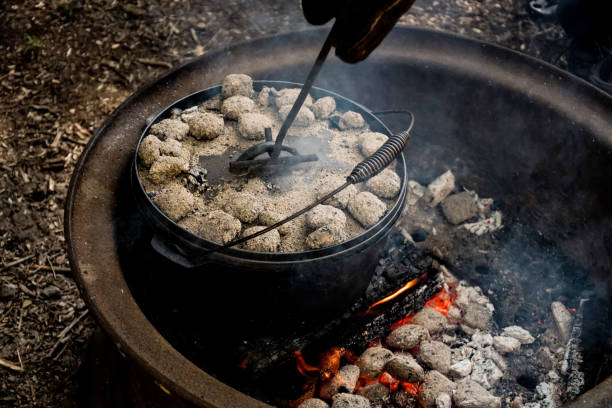 istock cast iron Dutch oven camp cooking with coal briquettes beads on top. Campfire in a firepit. Camping cooking 1409472251