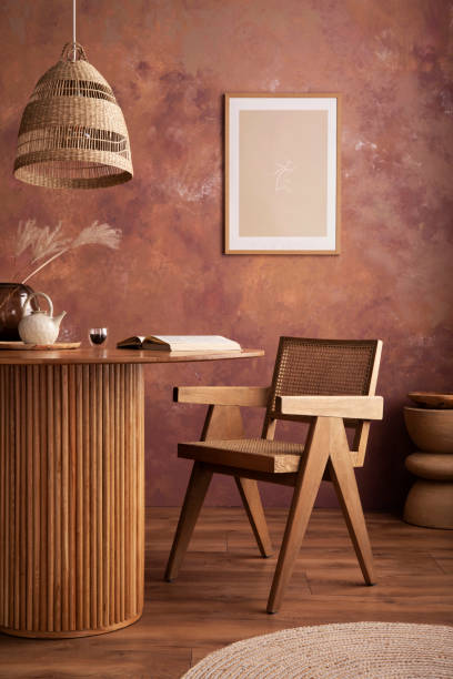 istock Stylish boho vintage dining room interior with poster mock up. Round table with rattan armchair, vase with dried flowers and cup. Brown wall and rattan lamp. Mock up poster. Template. 1409472268