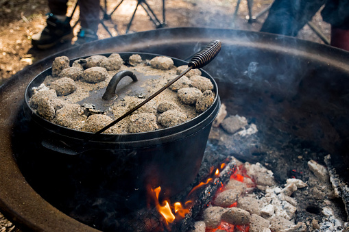 Dutch oven camp cooking with coal briquettes beads on top. Campfire in a firepit. Camping lifestyle