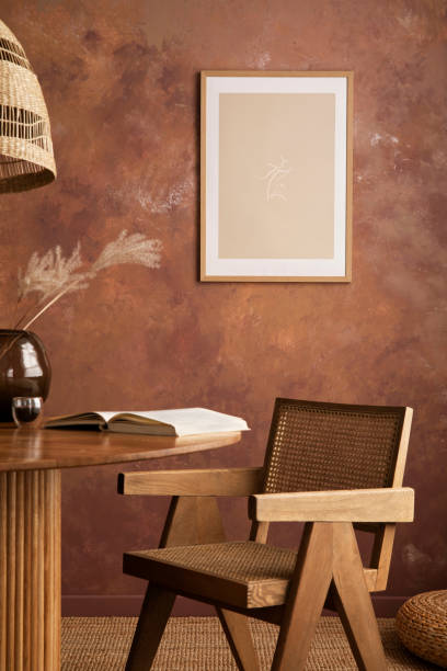 istock Stylish boho vintage dining room interior with poster mock up. Round table with rattan armchair, vase with dried flowers and cup. Brown wall and rattan lamp. Mock up poster. Template. 1409472366