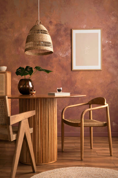 istock Domestic boho vintage dining room interior with poster mock up. Round table with rattan armchair, vase with dried flowers and cup. Brown wall and rattan lamp. Mock up poster. Template. 1409472406