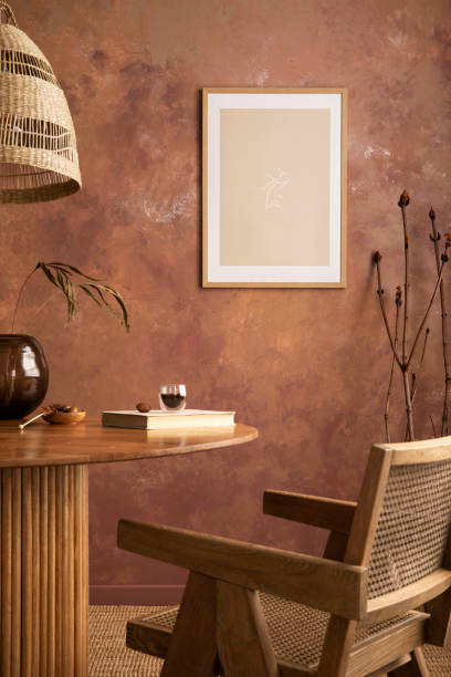 istock Cozy boho and vintage dining room interior with poster mock up. Round table with rattan armchair, vase with dried flowers and cup. Brown wall and rattan lamp. Mock up poster. Template. 1409472421