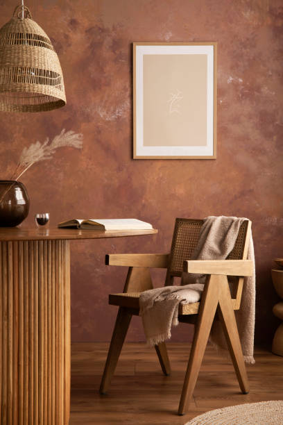 istock Stylish boho vintage dining room interior with poster mock up. Round table with rattan armchair, vase with dried flowers and cup. Brown wall and rattan lamp. Mock up poster. Template. 1409472423