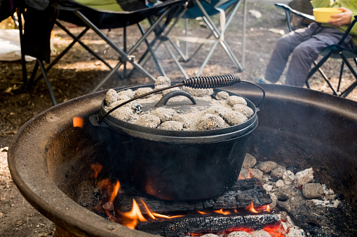 Dutch oven camp cooking with coal briquettes beads on top. Campfire in a firepit. Camping lifestyle