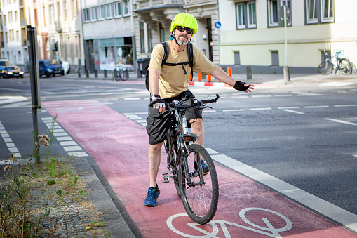 Male cyclist riding on a bike lane in the city center - giving a hand signal in order to turn left. Some unrecognisable traffic in the background.