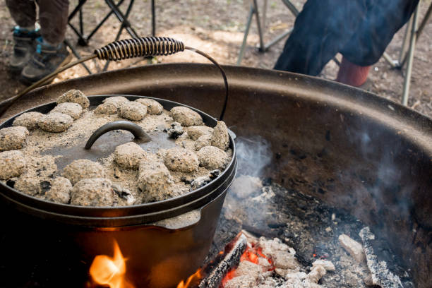 istock cast iron Dutch oven camp cooking with coal briquettes beads on top. Campfire in a firepit. Camping cooking 1409472580