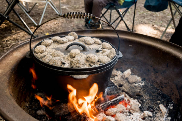 istock cast iron Dutch oven camp cooking with coal briquettes beads on top. Campfire in a firepit. Camping cooking 1409472608