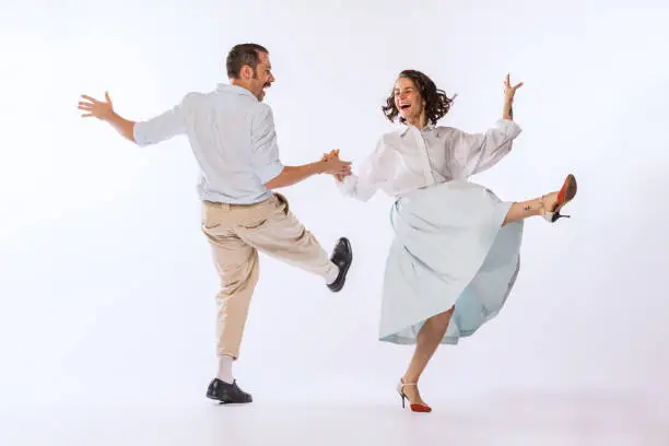 Photo of Portrait of young beautiful couple, man and woman, dancing retro dance isolated over white studio background. Enjoyment