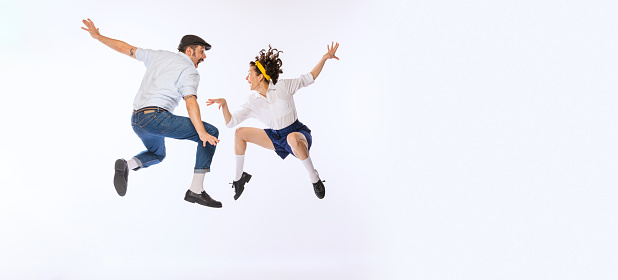 Portrait of young active couple, man and woman, dancing, jumping isolated over white studio background. Concept of vintage fashion, hobby, activity, art, music, party, creativity and ad