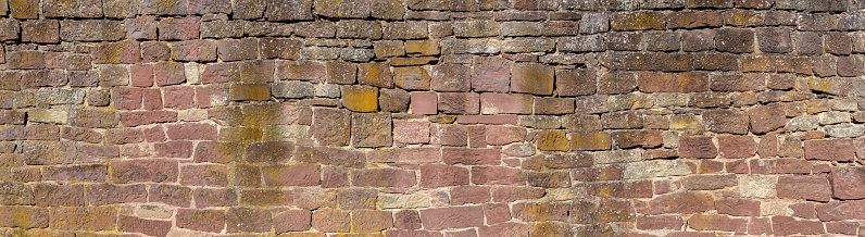 Old, heavily weathered panoramic stone wall made of different, square hewn natural stones