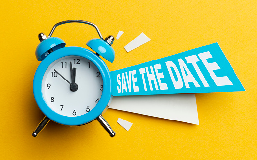 Blue alarm clock with colored papers and save the date text on yellow background.