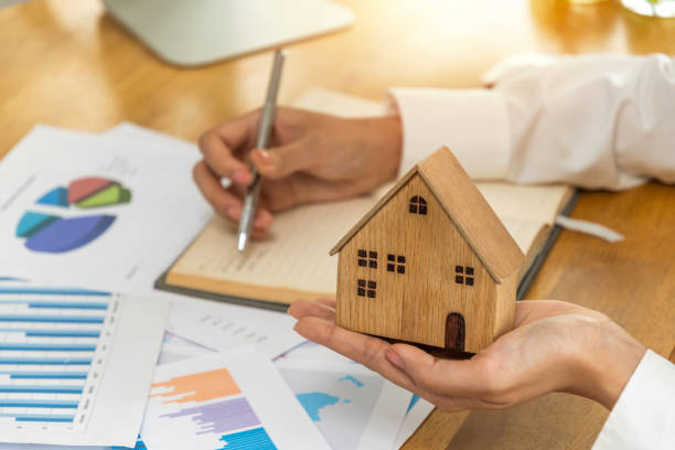 istock real estate broker manager holding house model and working and calculating about graph chart finance with document report on desk at home office, meeting, finance business, buy and sell house concept 1409475341