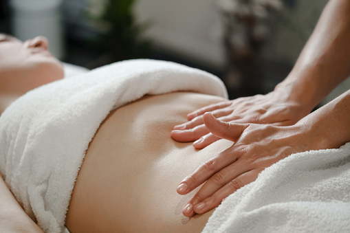 Top view of hands massaging female abdomen. Therapist applying pressure on belly. Woman receiving massage at spa salon, Japanese Chi Nei, Closeup