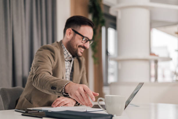 istock Smiling business professional enjoying coffee while working. Young entrepreneur is using laptop and taking a coffee break. 1409478044
