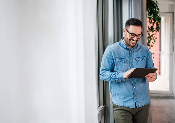 istock Smiling businessman wearing eyeglasses using computer tablet, standing in modern business space. 1409478050