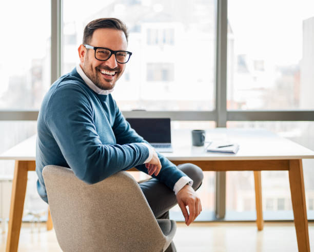 porträt eines jungen, lächelnden, glücklichen, gutaussehenden, erfolgreichen geschäftsmannes, unternehmers, freiberuflers, der rückblickend arbeitet. - desk men sitting computer stock-fotos und bilder