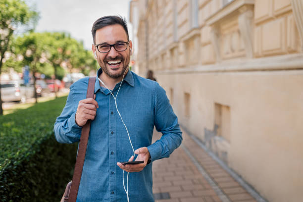 o viajante profissional masculino está ouvindo música de telefone inteligente. - mid adult men smart casual white happiness - fotografias e filmes do acervo