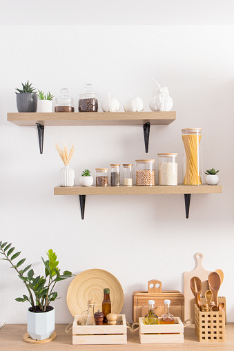 Open kitchen wooden shelves with jars for storage on a white textured wall and part of the countertop with environmentally friendly items for storage