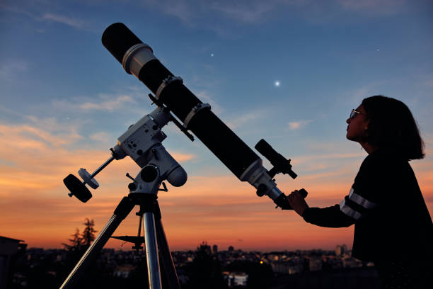 istock Girl with astronomical telescope stargazing under twilight sky. 1409485821
