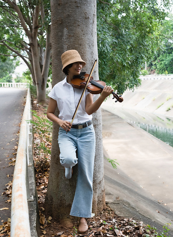 Woman wearing white shirt play violin with smiling face, in a park,hobby on holiday