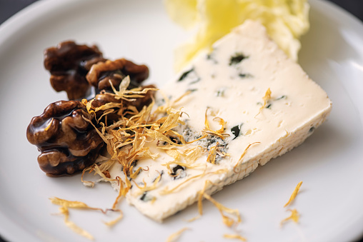 Fine dining cheese course. Creamy blue cheese with walnuts marinated in dandelion flower syrup and dried dandelion flower petals.