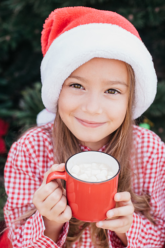 Merry Christmas. Portrait of funny child girl in Santa hat eating gingerbread cookies drinking hot chocolate outside having fun. Happy Holidays. kid enjoying holiday. Christmas in July