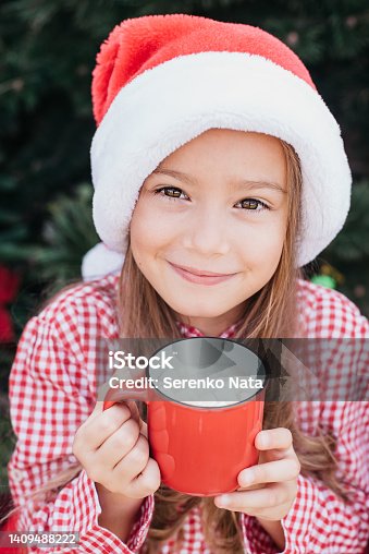 istock Merry Christmas. Portrait of two funny children girls in Santa hat eating gingerbread cookies drinking hot chocolate 1409488222