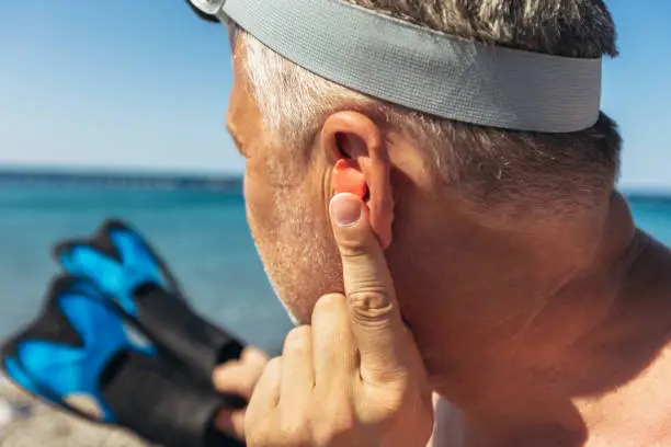 Mature man putting silicone ear plugs, surfers earplugs, swim plugs