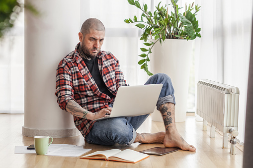 Mid adult freelance worker surfing the Internet on a computer on floor at casual office.